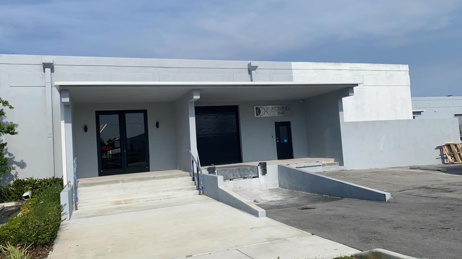 Completed light gray commercial warehouse loading dock repaint with black roll-up doors in Miami