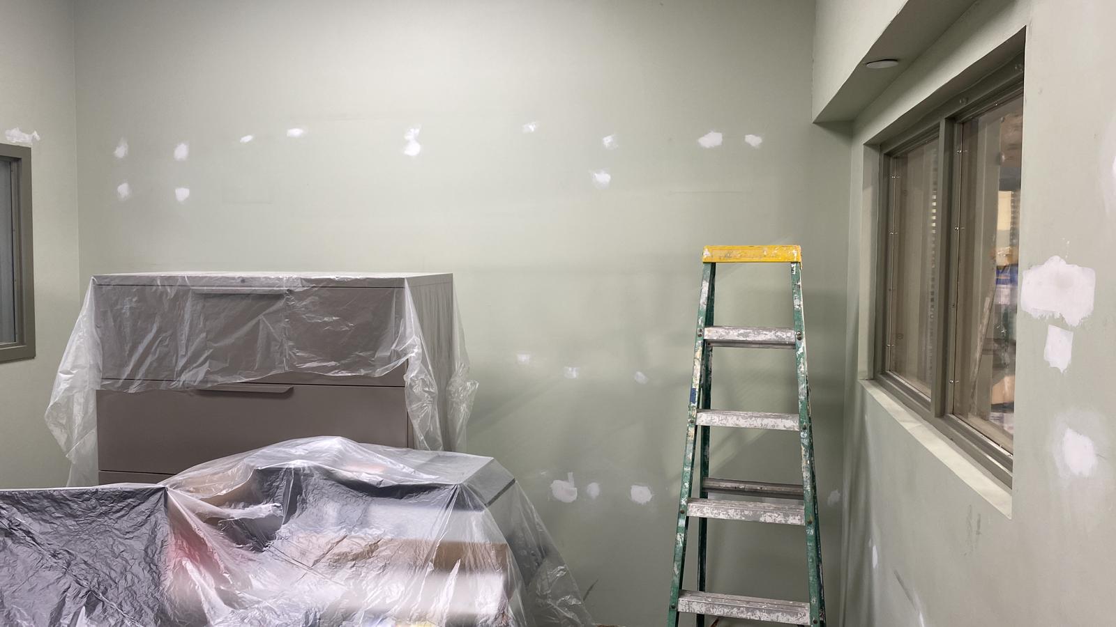 Sage green office interior with furniture covered in plastic and drywall spot repairs before painting in Doral