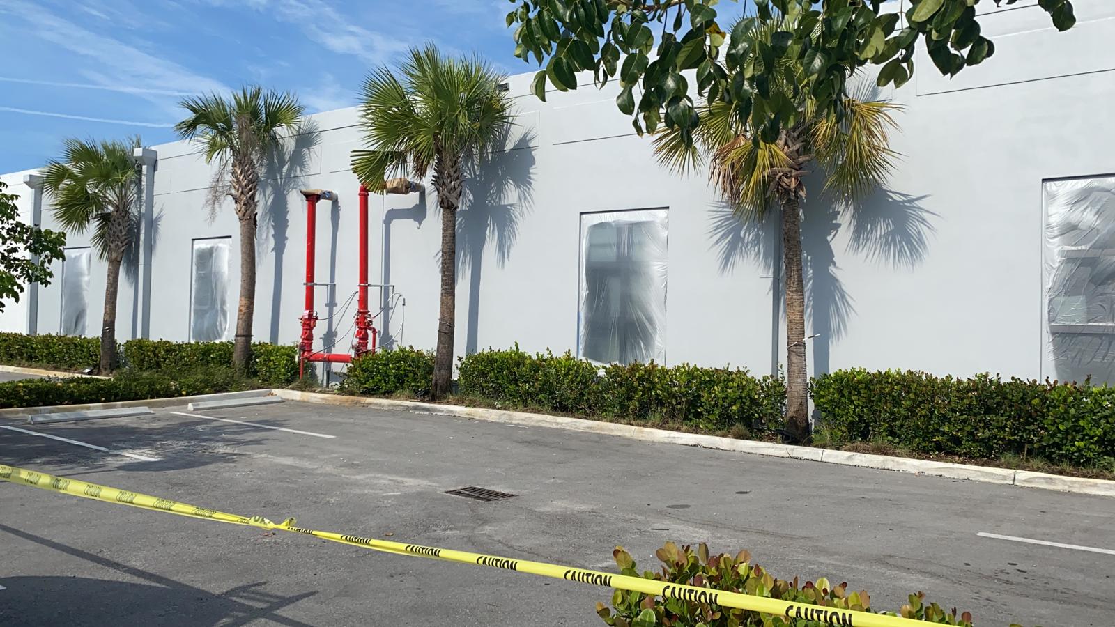 White commercial warehouse exterior with windows masked in plastic sheeting during a Pompano Beach repaint project