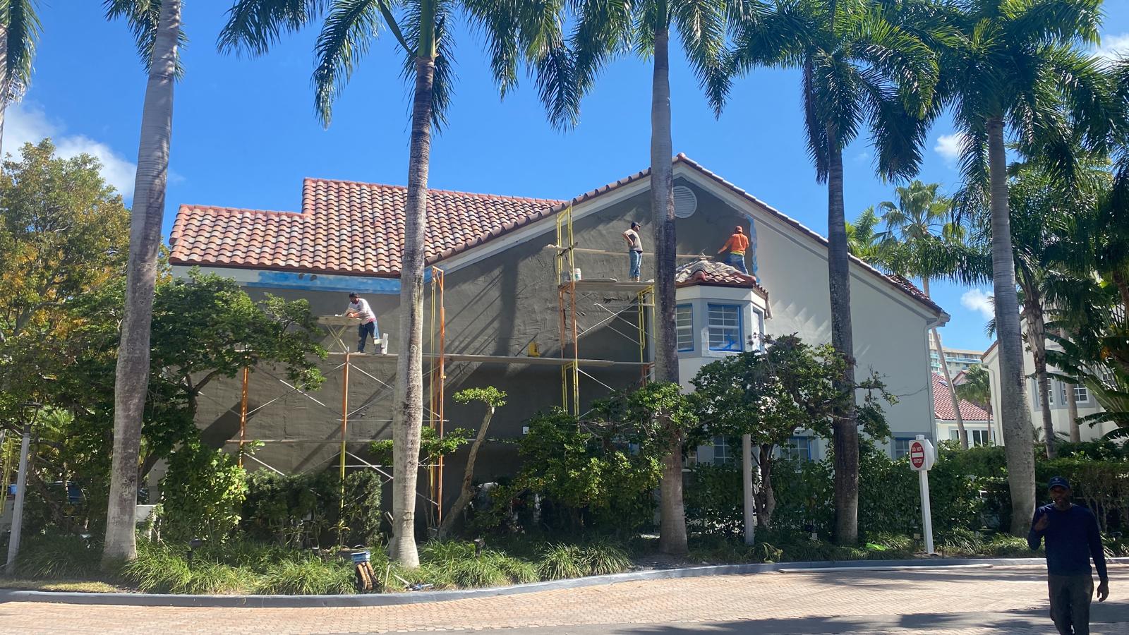 Painting crew on scaffolding repainting a two-story stucco home exterior in Boca Raton Florida