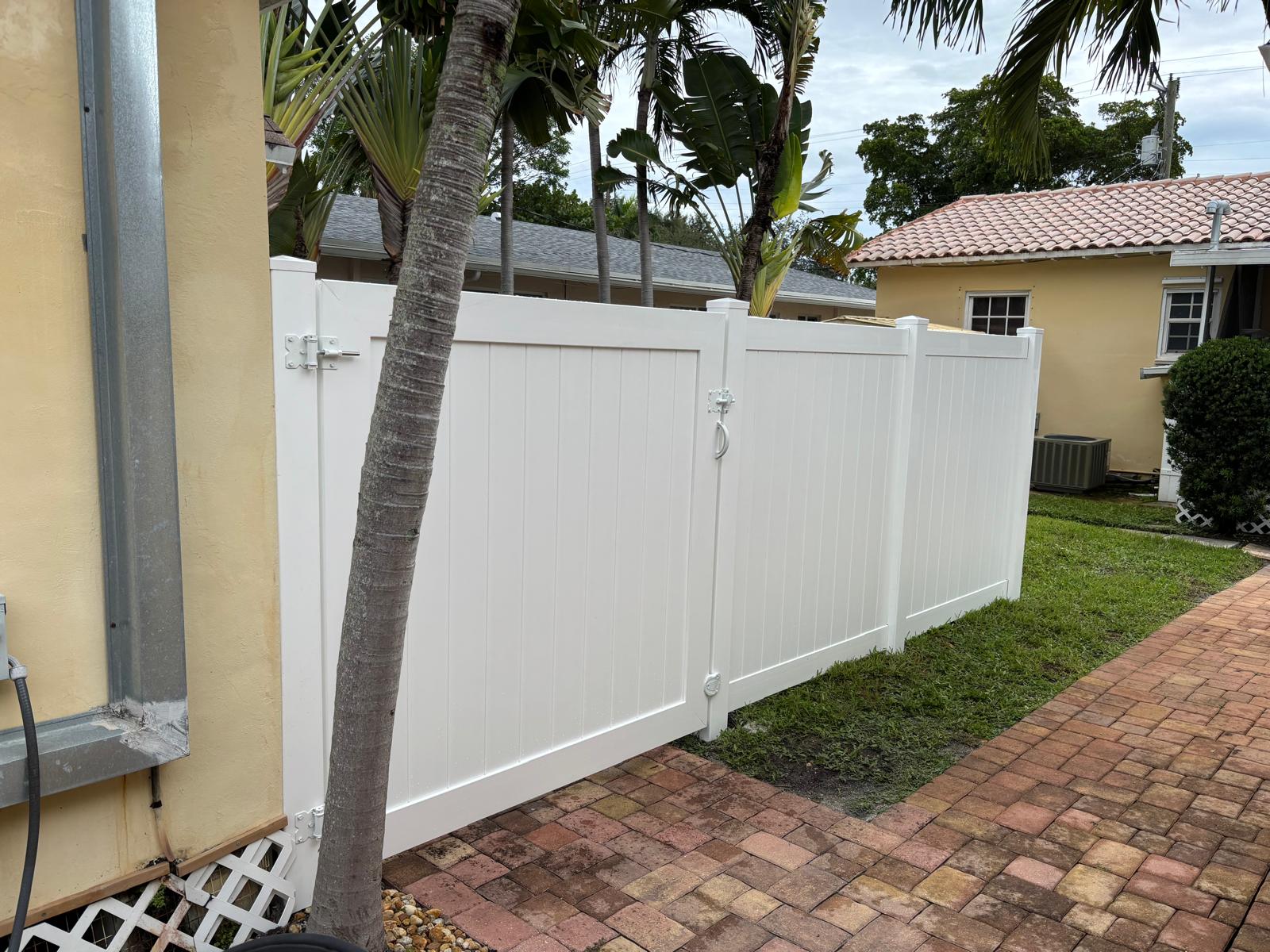 White vinyl fence and gate painted around a Miami residential home with paver walkway