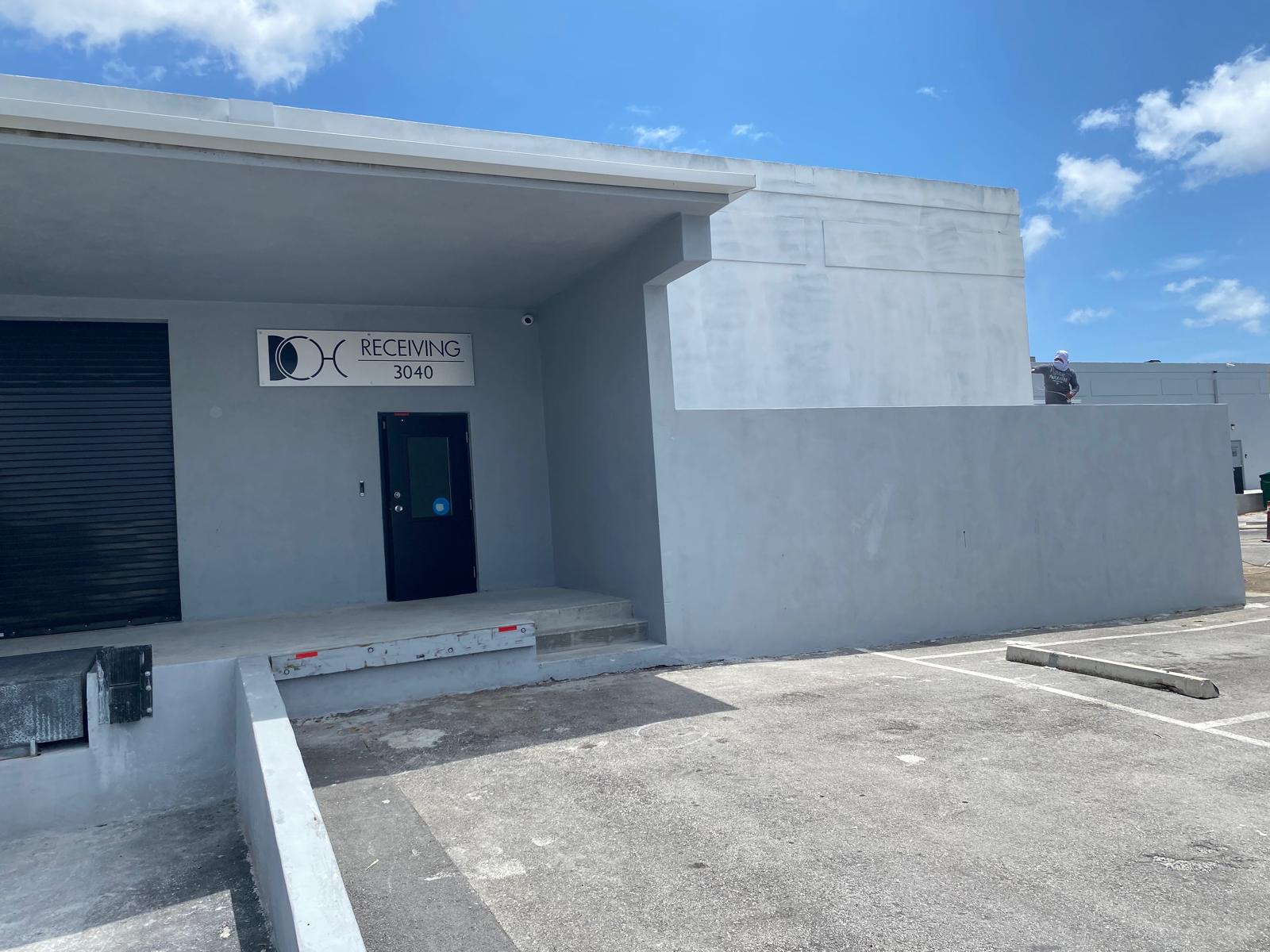 Gray commercial receiving dock exterior repaint with painter on wall at a Miami industrial building