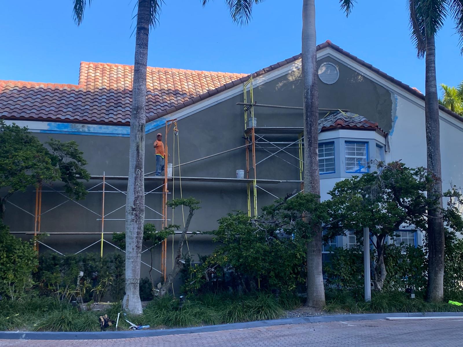 Painter applying primer coat on the exterior stucco wall of a two-story home in Aventura Florida